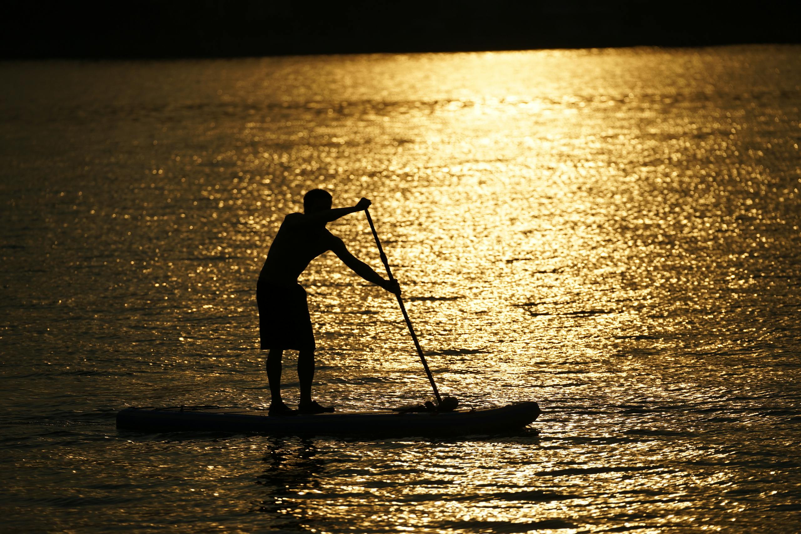 A silhouette of a person paddleboarding at sunset in Hanoi, Vietnam, creating a serene and golden reflection over the water.